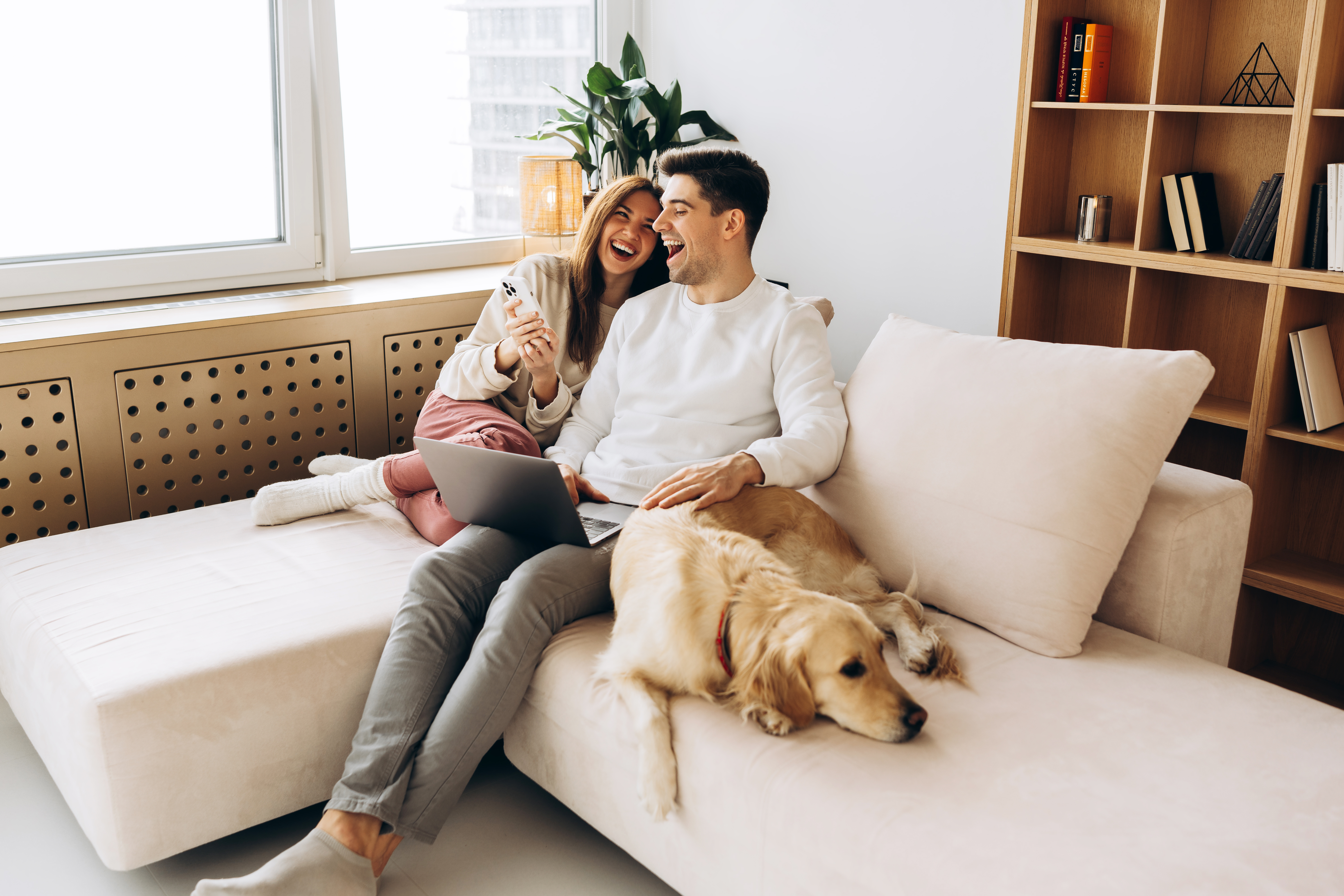 A golden retriever resting beside a couple on their cream sofa